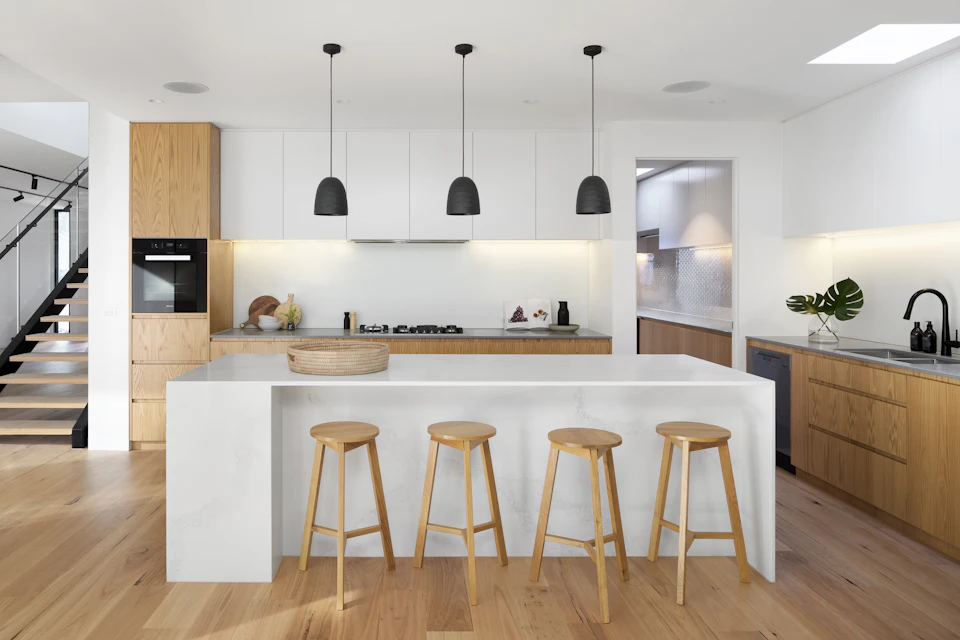 A bright kitchen with a long island, timber cabinetry and four stools